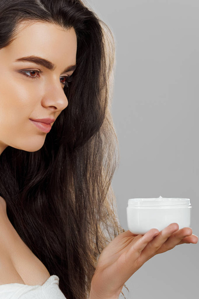 Skincare. Beauty Concept. Young pretty woman holding cosmetic cream. Soft skin and naked shoulders,model with light nude make-up, portrait of female holding moisturizing cream in her hand. Skin Protection and dermatology. - Foto, Imagen