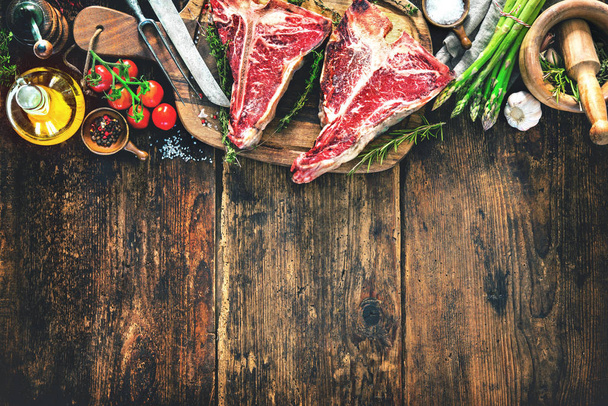 Raw dry aged t-bone steaks for grill with fresh herbs and vegetables on rustic wooden board - Φωτογραφία, εικόνα