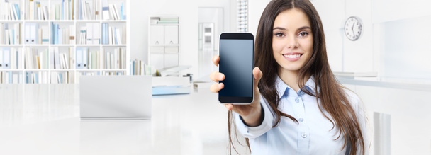 Hymyilevä nainen näyttää älypuhelin eristetty sisätilojen toimisto liiketoiminnan tausta
 - Valokuva, kuva