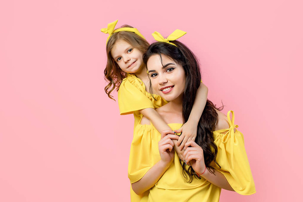 Young woman with cute child posing in yellow dresses - 写真・画像