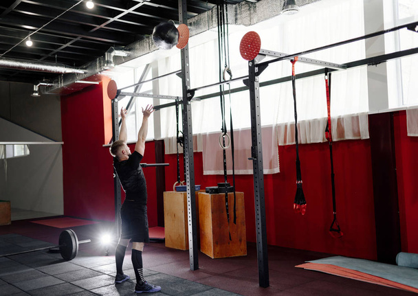 muskulöser Mann beim Turnen mit Medizinball im Fitnessstudio. junger Mann macht Oberkörpergymnastik mit schwerem Ball - Foto, Bild