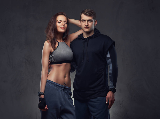 Attractive couple, slim brunette female and handsome guy in sportswear cuddling in a studio. Isolated on a dark background. - Foto, Imagem