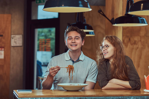 Happy νεαρό ζευγάρι φορούν casual ρούχα, τρώνε πικάντικα νουντλς σε ένα ασιατικό εστιατόριο. - Φωτογραφία, εικόνα