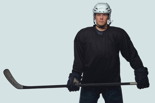 Hockey player wearing black protective gear and white helmet holds a hockey stick. Isolated on a gray background. - Photo, Image