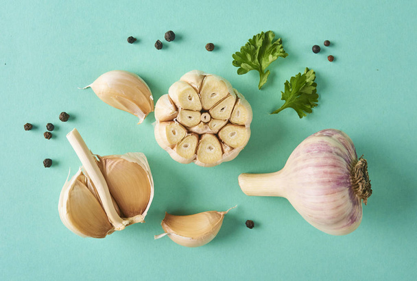Concepto de comida. Composición con ajo fresco, hojas de cilantro y pimienta aisladas sobre fondo turquesa
 - Foto, Imagen