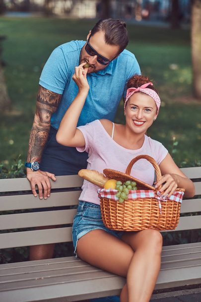 Ελκυστική μέση ηλικία ζευγάρι κατά τη διάρκεια του ραντεβού, απολαμβάνοντας ένα πικ-νικ σε ένα παγκάκι στο πάρκο. - Φωτογραφία, εικόνα
