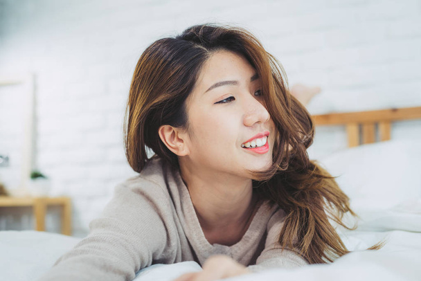 Portrait beautiful young Asian woman on bed at home in the morning. Cheerful Asian woman wearing a comfortable sweater and smiling on her bed. Relaxing room. lifestyle asia woman at home concept. - Photo, Image