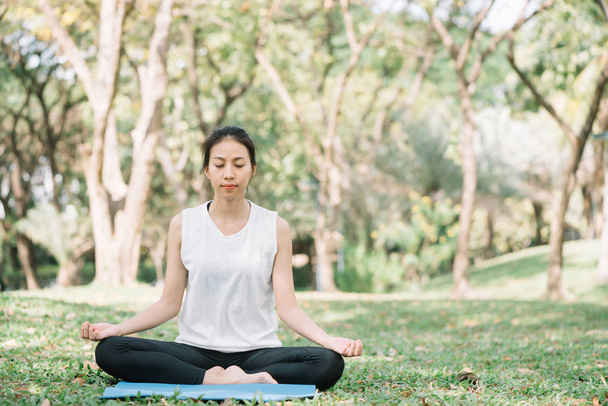 Young asian woman yoga outdoors keep calm and meditates while practicing yoga to explore the inner peace. Yoga and meditation have good benefits for health. Yoga Sport and Healthy lifestyle concept. - Photo, Image