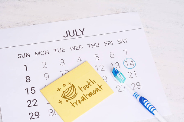 Calendar with a marked date and toothbrush to remind dentist appointment day in july. Dental hygiene and healthy concept. - Photo, Image