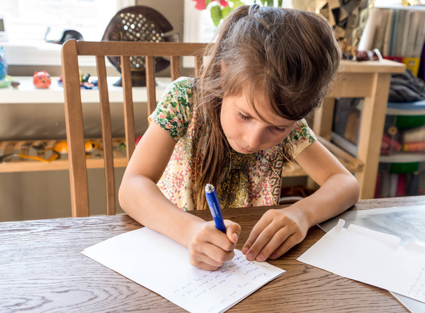 Dziewczyna pisze jej pracę domową na białej kartce papieru długopisem - Zdjęcie, obraz
