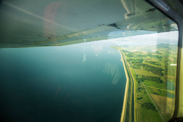 Piękny krajobraz aero, patrząc z okna samolotu małe pod skrzydła. Ryga, Łotwa, Europa w okresie letnim. Autentyczne doświadczenie latające w dzień słoneczny, zamglony. Krajobraz z powietrza. - Zdjęcie, obraz