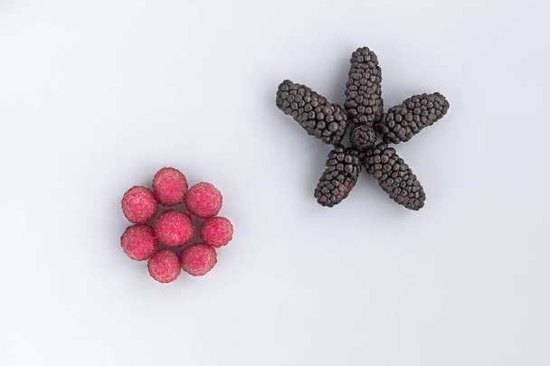 Zralé plody malin a velká černá blackberry jsou umístěny diagonálně na světlém pozadí, obrázek v vysoký klíč - Fotografie, Obrázek