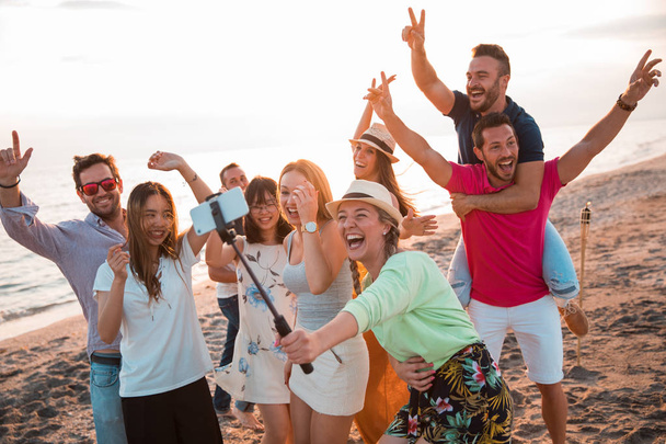 Happy multiracial young people are making a selfie at the beach while they are in a summer party. Friends and holiday concept - Φωτογραφία, εικόνα