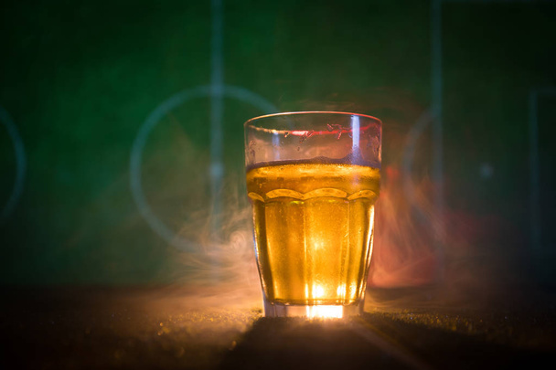 Δημιουργική ιδέα. Ποτήρι φρέσκια μπύρα στο γρασίδι με θολή στάδιο σε φόντο με ομίχλη και το φως. Ποτήρι μπύρας lager έτοιμο για ποτό. Αντιγράψτε το χώρο. Επιλεκτική εστίαση - Φωτογραφία, εικόνα