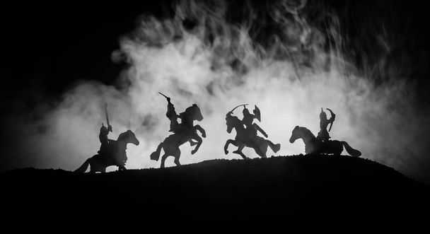 Средневековая боевая сцена с кавалерией и пехотой. Силуэты фигур как отдельные объекты, борьба между воинами на темном, тонированном туманном фоне. Ночная сцена. Селективный фокус
 - Фото, изображение