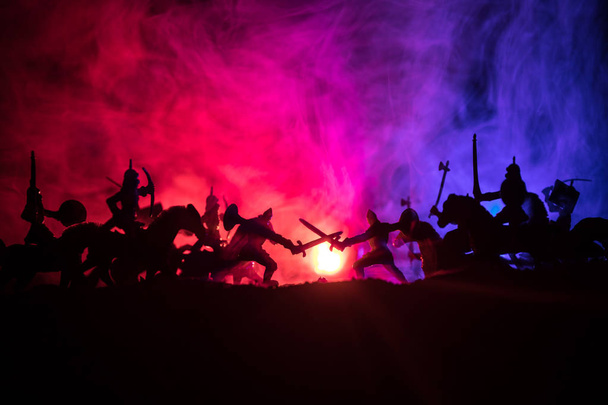 Medieval battle scene with cavalry and infantry. Silhouettes of figures as separate objects, fight between warriors on dark toned foggy background. Night scene. Selective focus - Photo, Image