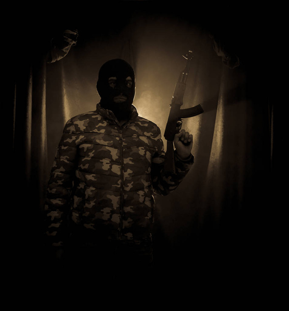 Silhouette de l'homme avec fusil d'assaut prêt à attaquer sur fond brumeux sombre ou dangereux bandit en noir portant de la cagoule et tenant pistolet à la main. Tir terroriste avec décor de thème d'arme
 - Photo, image