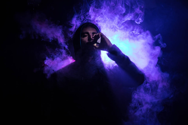 Vaping man holding a mod. A cloud of vapor. dark foggy toned background of clouds of smoke. Vaping an electronic cigarette with a lot of smoke. Vape concept. Selective focus - Foto, afbeelding