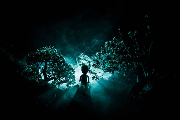 Horror Halloween utrzymane obraz koncepcyjny. Sama dziewczyna z światło w lesie w nocy. Sylwetka dziewczynę stojącą między drzewami z surrealistyczne światło na tle. Selektywny fokus. - Zdjęcie, obraz