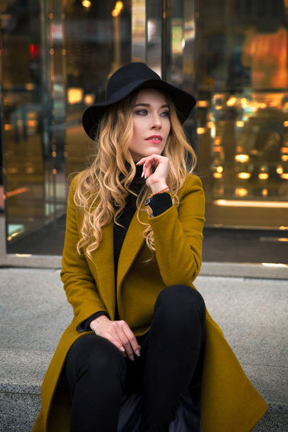 オリーブ コートと黒のつばの広い帽子を身に着けている若い美しいファッショナブルな女性の屋外のポートレート。よそ見モデル。女性のファッションのコンセプトです。都市生活。クローズ アップ. - 写真・画像