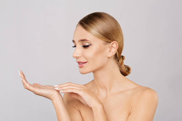 Portrait of smiling beautiful blonde woman showing empty copy space on the open hand palm.Proposing a product.Beauty young woman with fresh clean perfect skin.Skin care concept.Facial treatment - 写真・画像