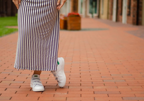 Woman in dress female legs in street sneakers on blur background beauty fashion - Foto, Imagem