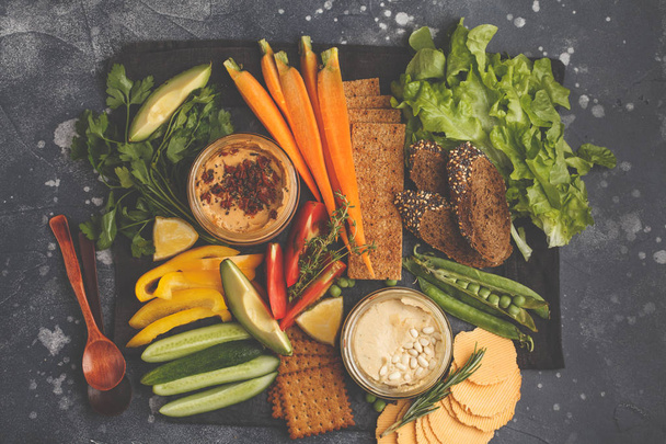Vegetarian Arabic dip hummus with vegetables and different snacks on a dark background. Healthy vegan food concept. - Fotografie, Obrázek