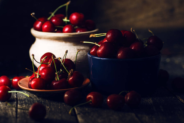 still life picture in the dark of fresh cherry on plate on wooden black background. fresh ripe cherries. soft focus image  - Фото, изображение