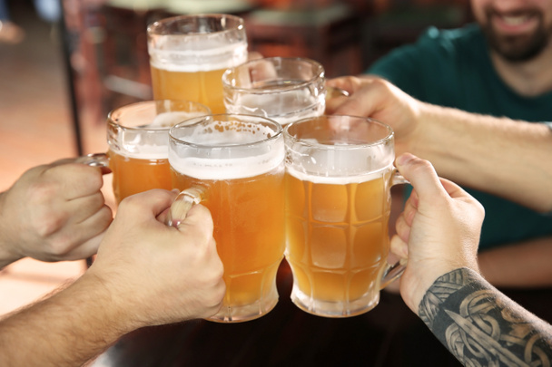 Amigos tintineando vasos con cerveza en el pub
 - Foto, imagen