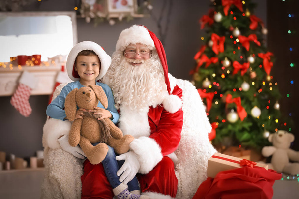 Little boy with toy bunny sitting on authentic Santa Claus' lap indoors - Foto, Bild
