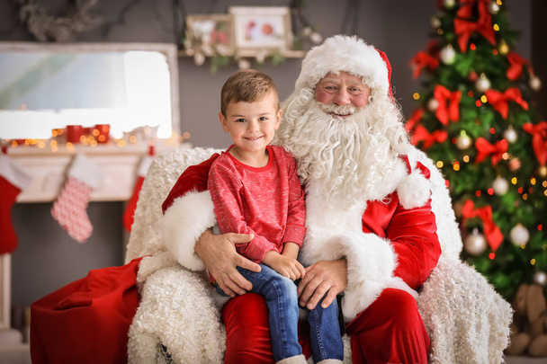 Little boy sitting on authentic Santa Claus' lap indoors - 写真・画像