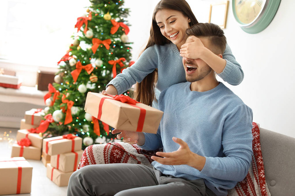 Young woman surprising her boyfriend with Christmas gift at home - Fotó, kép