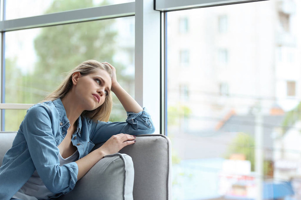 Νεαρή γυναίκα λυπημένος που κάθεται κοντά στο παράθυρο στο σπίτι - Φωτογραφία, εικόνα