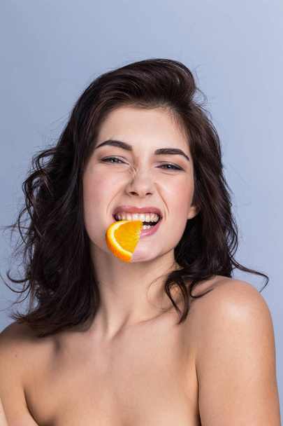 Young funny woman biting slice of orange, healthy eating concept - Фото, изображение