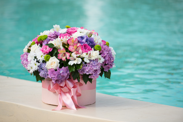 un beau bouquet dans une boîte se trouve au bord d'une piscine avec de l'eau bleue
 - Photo, image