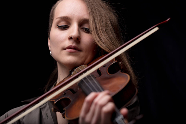 серйозний і концентрований скрипаль - портрет жінки на чорному тлі, що грає струни
 - Фото, зображення