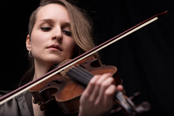 serious and concentrated violin player - portrait of a woman on black background playing strings - Foto, Imagen