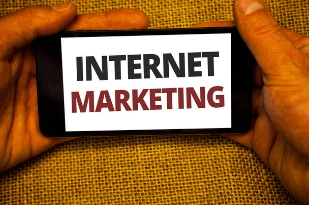 Text sign showing Internet Marketing. Conceptual photo Online Commerce Networking Entrepreneur Entrepreneurship Jute sack background hand holding iPhone with colorful alphabetic syllable - Photo, Image