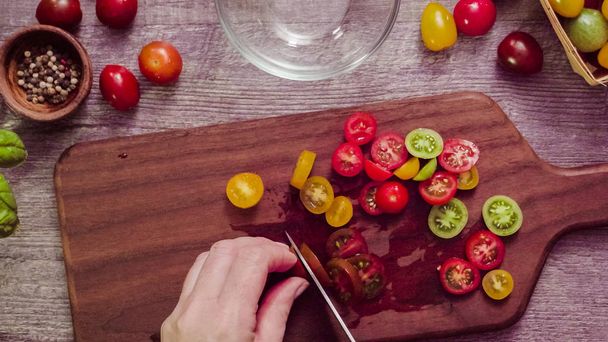 Step by step. Slicing heirloom cherry tomatoes on wood cutting board. - 写真・画像