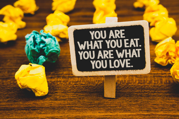 Text sign showing You Are What You Eat. You Are What You Love.. Conceptual photo Start to eat healthy food Blackboard with letters wooden floor blurry yellow paper lumps green lob - Photo, Image