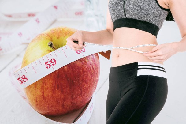 Woman slim measuring her waist using a tape measure on apple and measuring tape - healthy eating and dieting concept - Foto, Imagen