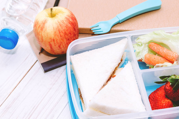 Lunch box with vegetables and slice of bread for a healthy school lunch on wooden table - Foto, imagen