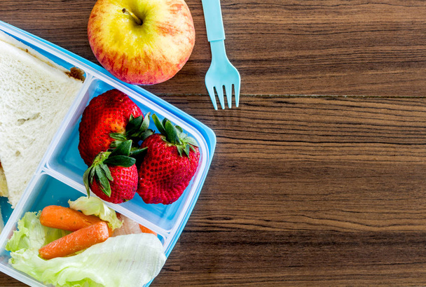 Обеденная коробка с овощами и ломтиком хлеба для здорового школьного обеда на деревянном столе
 - Фото, изображение