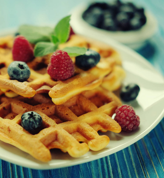 belgian waffles with fresh berrys and sugar powder on white plate, blue wooden background. Flat lay, top view, copy space. Close up. - Fotografie, Obrázek