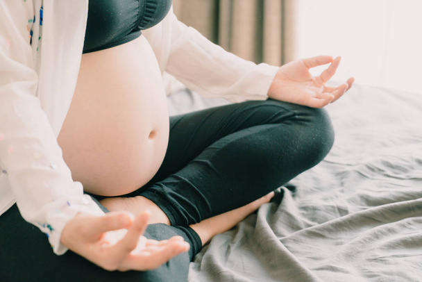 Jovem bela mulher grávida asiática meditando ou fazendo exercício de ioga em casa. Relaxamento ioga postura de lótus. - ponto de foco seletivo e estilo vintage
 - Foto, Imagem