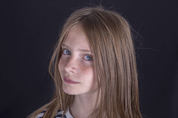 Beautiful blond young girl with freckles indoors on a black background, close up portrait - Zdjęcie, obraz
