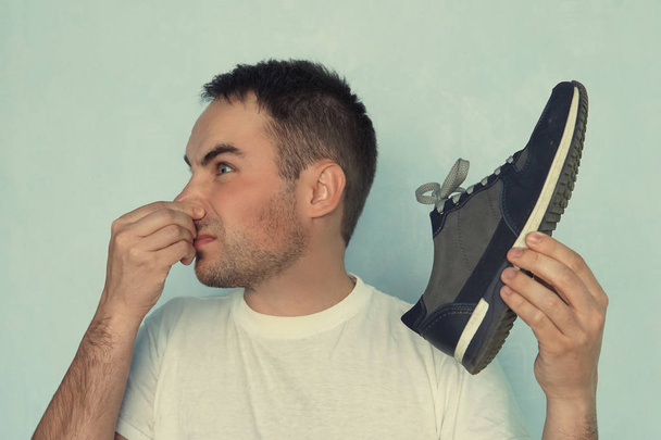 Bir adam elinde tuttuğu spor ayakkabısından yayılan koku yüzünden burun deliklerini sıkıyor.. - Fotoğraf, Görsel