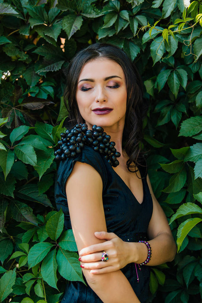 Portrait of young sexy brunette in black dress with black grapes. . - Fotografie, Obrázek