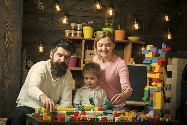 family leisure. Kid with parents play with plastic blocks, build construction. Father, mother and cute son play with constructor bricks. Family on busy faces spend time together in playroom. Family - Photo, Image