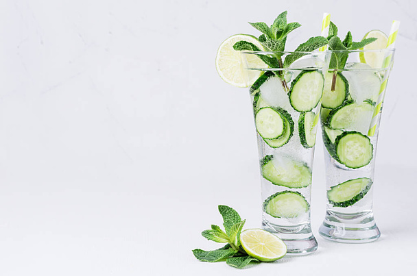 Mineral water with slices cucumber, ice, lime, mint on white wood table with copy space. Fresh summer cool fitness cocktail. - Zdjęcie, obraz